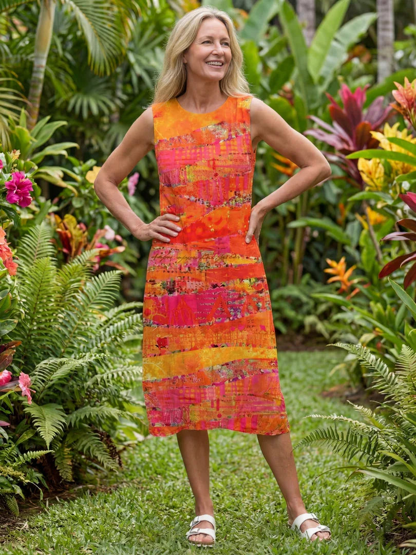 Woman in vibrant orange pink abstract print sleeveless dress, standing in lush tropical garden